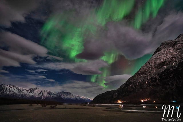 Northern Lights in bright shades of green with some clouds mixed in as seen above the Knik River and Pioneer Peak.