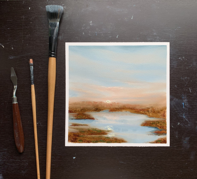 Original sunrise marsh painting by Tisha Mark, "Monday Morning at the Marsh" 8"x8" oil on Arches paper (2024), shown with brushes and palette knife for scale. An early spring marshland at sunrise, with sunlight and colors (oranges and blues) from the sky reflecting in water.