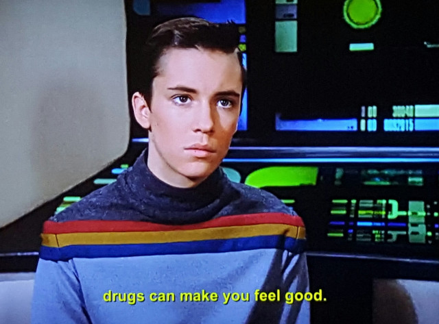 Young ensign Wesley Crusher sits at a console on the bridge, but he's turned around like he's having a talk with safe adult who has walked up behind him. He looks sincere and earnest, as if it's a 'very special episode of Star Trek: The Next Generation.' He's wearing his blue and blue and gold and red and blue again Wesley sweater, which is not a bad look, tbh. Closed caption reads, "drugs can make you feel good."