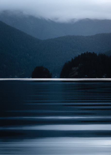 A blue hour photograph of Jug Island, taken from across the water in Deep Cove in North Vancouver, BC. The island is central in the portrait-oriented frame, and ripples have been caught coming in towards the camera.
