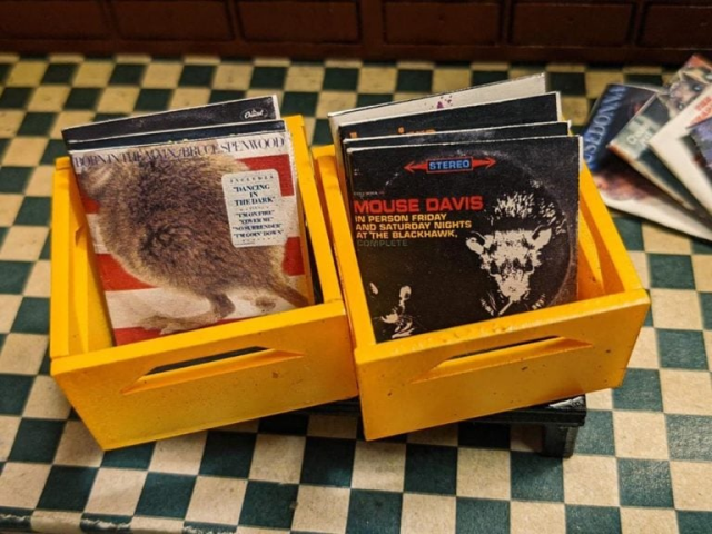 Two teeny yellow record crates filled with mouse-themed versions of well-known album covers sit on a blue & white checked floor.