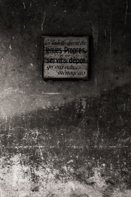 A wooden sign on an old decaying wall advises residents that the bins should be kept clean and only used for household refuse. Monochrome.