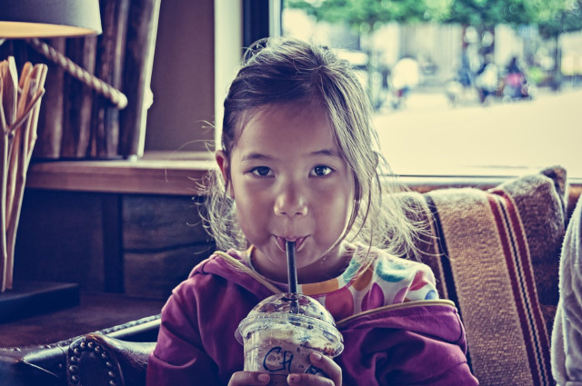 A small girl drinking chocolate from a plastic cup with a straw.