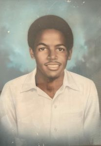 High school photo portrait of James Earl Green. He has a slight smile, dark brown skin, and medium length hair, and is staring just past the camera. He's wearing a white button up shirt. 