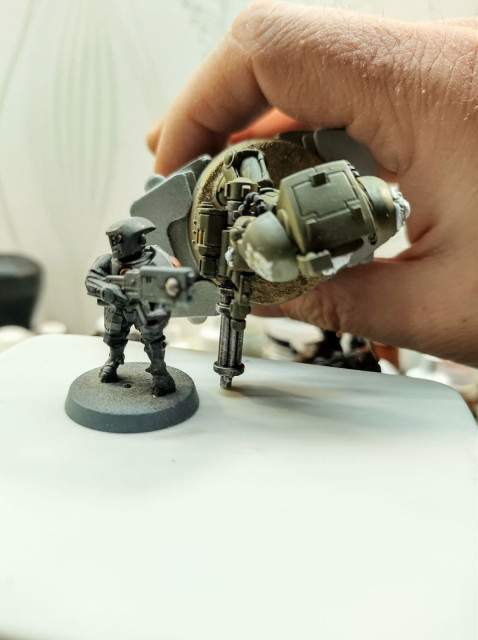 A Tau Fire Warrior next to a Terminator assault cannon. The cannon is bigger than the Tau model.