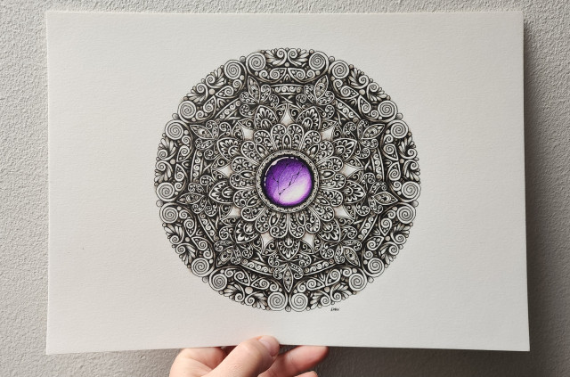 An intricate black ink shaded mandala with repeating patterns of detail-filled leaves and swirls, surrounding a central vibrant purple cracked gemstone. My hand is holding up the paper against a white wall.