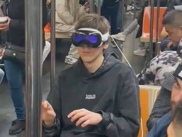 A nerd with an Apple Vision Pro strapped to his head on the NY subway, looking like a total fool.