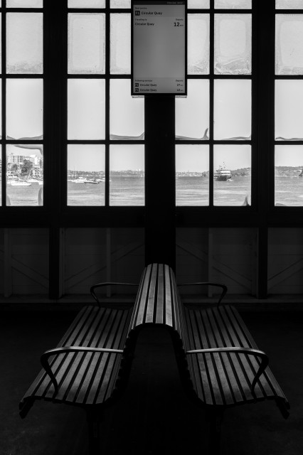 Black and white photo of a bench in front of windows at a ferry wharf in Sydney. 