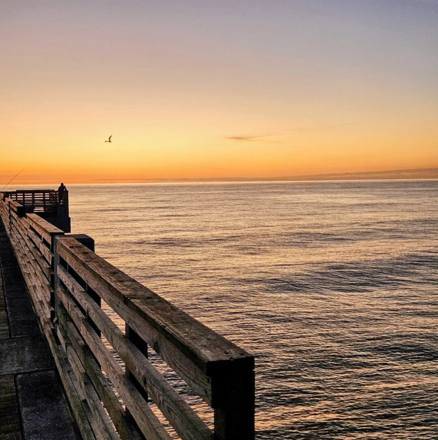 Layers of different yellow and orange shades line the horizon over the vast ocean view atop a beachside fishing pier.