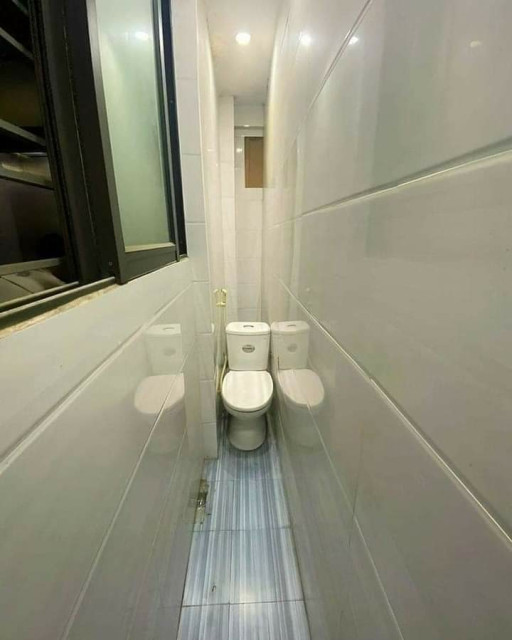 A toilet that is situated at the end of a extremely narrow hallway that is barely wide enough for one person to walk through.