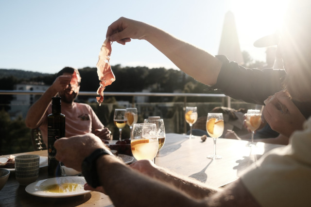 People enjoying some drinks outdoors, a person holding a piece of Jamón ibérico.