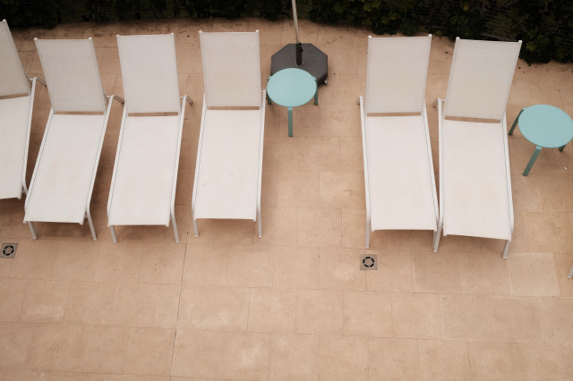 Overhead view of an outdoor area with white sun loungers and small turquoise tables on a tiled patio.
