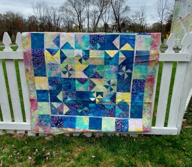 a quilt, it is done with soft hand-dyed fabrics, bright and colorful, there are cross-wheels of blue on a blue and yellow background, really fresh and tropical looking 