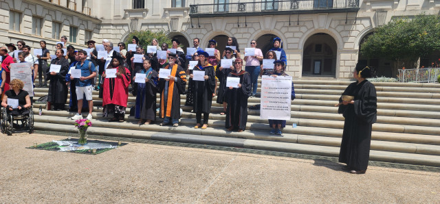 Protesters hold up signs with names of people killed in Gaza, and facts about the "scholasticide" including hundreds of destroyed schools. Many are dressed in their academic robes. 
