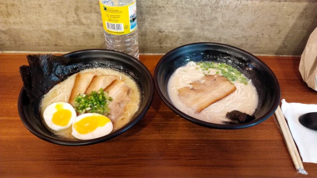 Two bowls of ramen from Kyukyu Ramen. The one on the left has more pork slices and has two halves of soft-boiled egg