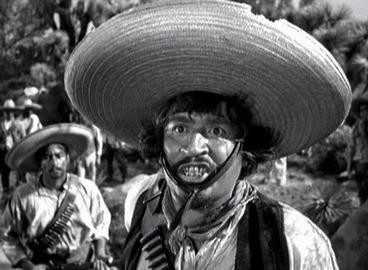 Stereotypical "Mexican bandit" with bad teeth, wearing a sombrero and a bandolier of bullets, in scene from "The Treasure of Sierra Madre."
