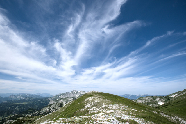 Am Berg mit Blick über einen langgezogenen Grat und Wolken, die sich in dieselbe Richtung nach hinten verjüngen.