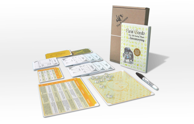 Photograph of the content of the "Paris Gondo - The Life-Saving Magic of Inventorying" boxset that include a rule book and dry-erase play-aids and adventurer card decks. 