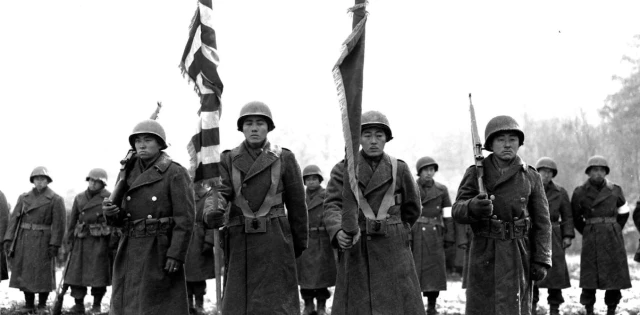 Members of the Japanese American 442nd Regimental Combat Team standing at attention with a furled US flag in Bruyères, France.