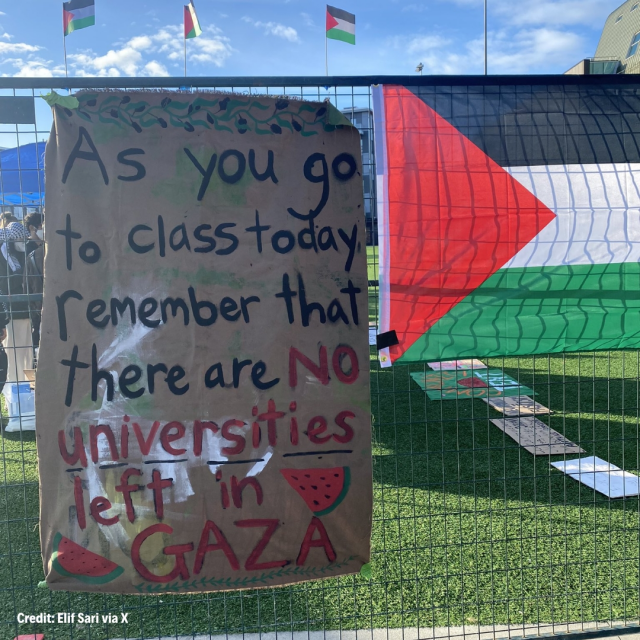 Cardboard sign on a fence, next to a Palestine flag reads:
As you go to class today remember that there are no universities left in Gaza.