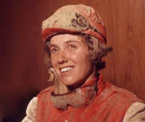 Diane Crump in muddy jockey gear after riding the race. She is a white woman with fair hair.