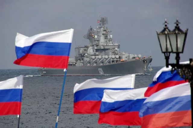 Un navire de guerre en mer avec plusieurs drapeaux russes au premier plan.