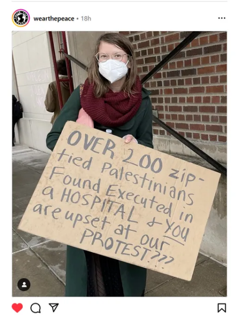 A woman wearing a mask &  holding a hand written placard with the words "Over 200 zip-tied Palestinians found executed in a HOSPITAL and you are upset at our PROTEST???'"