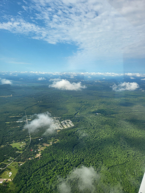 Small clouds over a dense forest with a small neighborhood cut out of it.