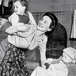 Marguerite 'Peggy' Knight after world war two, with a toddler on her back and a baby sat before her. She is a white woman with dark hair.