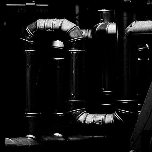 dunkles Bild einer Rohrinstallation, wo nur die vom Tageslicht angeleuchteten Rohrverkleidungen zu sehen sind.