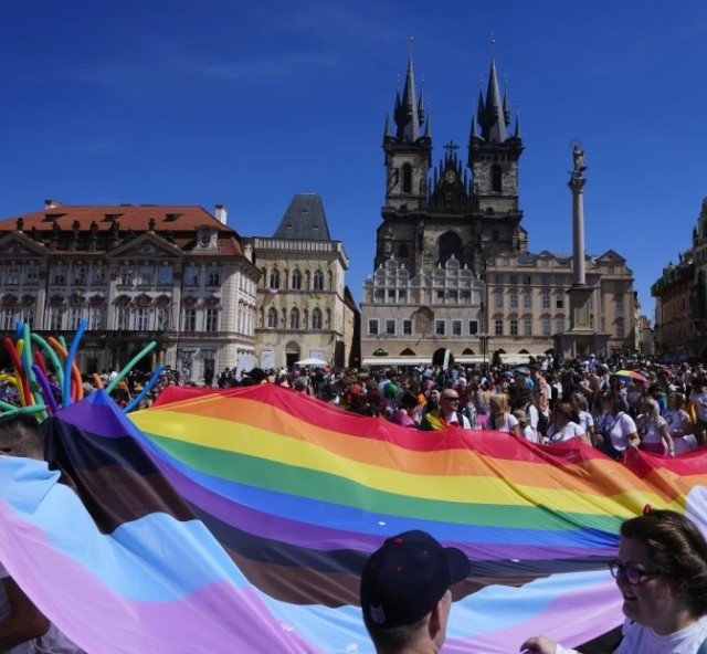 Rainbow flag including transgender colors being held by a crowd on the Old Town square in Prague