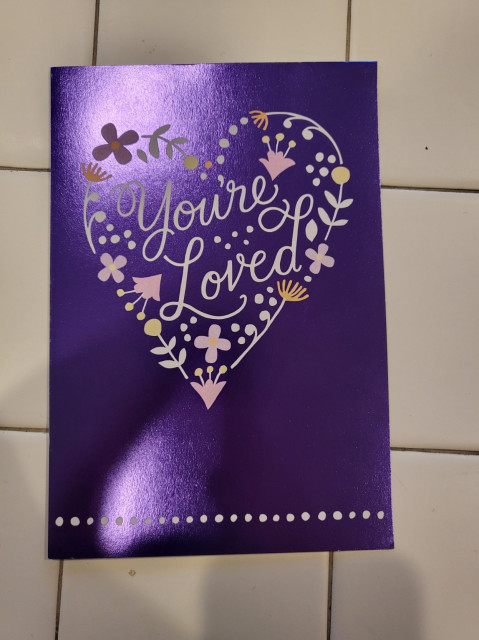 A purple greeting card that says "you're loved" on the front.