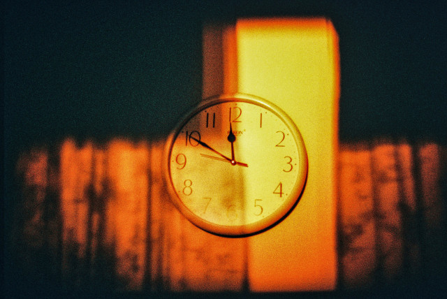Close-up of a round clock hanging on a wall in a room. The clock reads 11:50 a.m.
Sunlight from a window on the opposite wall is shining on the wall and the clock, turning it orange.