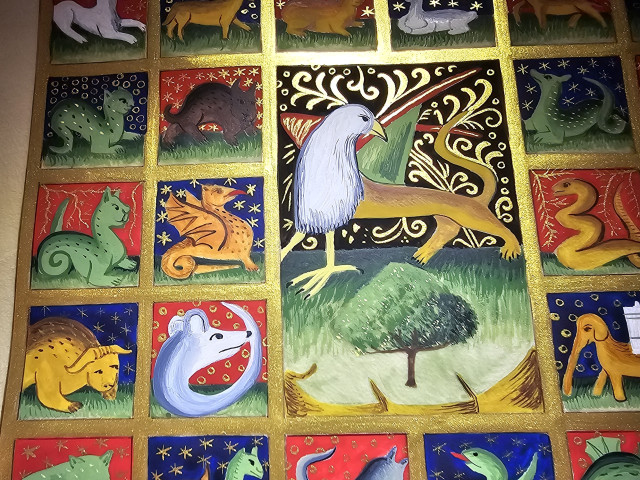 Close up picture of the illuminated bestiary. You can see blue and red vignettes, with fantastic beasts inside. The central vignette shows a griffon on a black and gold background (a beast with an eagle head, a lion body and dragon wings). They are all contained in a golden grid.