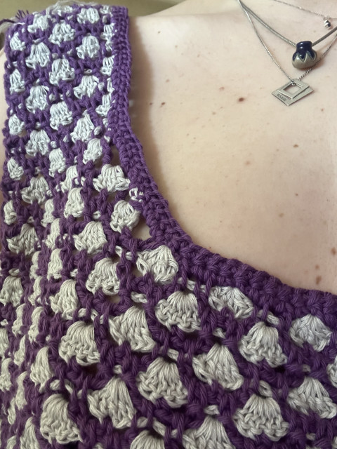 Detail view of a crochet top with violett yarn surrounding white clamshells pointing downwards