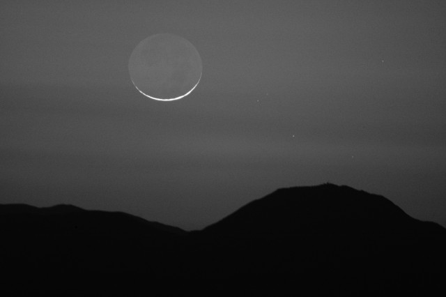 Infrared view of a one-day old moon that is below one degree elevation. It is not a circle. It has a squashed appearance because of atmospheric refraction.

A few of the stars of the Pleiades are visible to the right and down from the moon.

Haze and dust layers are prominent.

The mountain range is 45 miles away.