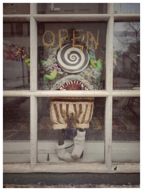 Fenster eines Geschäftes, hinter den geteilten Scheiben steht eine Monsterpuppe mit aufgerissenem Mund. Oben steht OPEN.