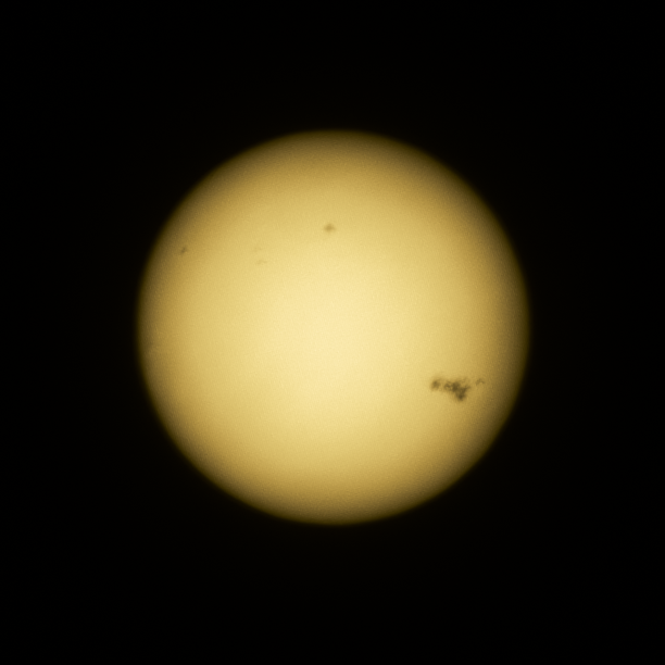A picture of the Sun taken with a DSLR camera through crossed polarisers to make it faint enough. There are several dark sunspots seen on the Sun, including a very large group to the righthand side.