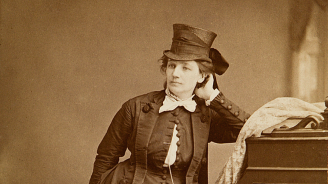 1870 photo of Victoria Woodhall. She is a white woman with dark hair, wearing a top hat and victorian-era clothing.