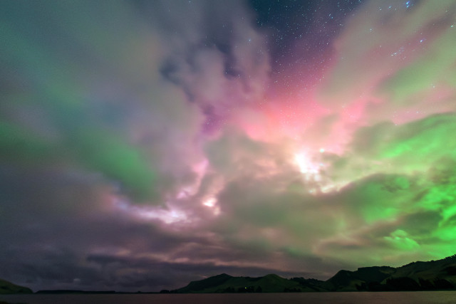 A pastel aurora glows behind clouds 