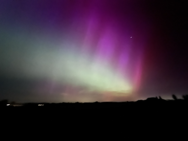 Large view over the fields of the northern lights. A wave of green and pink on top over the dark silhouette of the horizon 