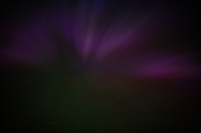 A dark photo looking upwards to the night sky, showing the Aurora Borealis.
The colours are magenta on the top half, and a feint green bottom half.
