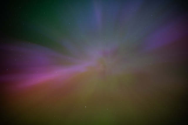 A very colourful photo looking upwards to the night sky, showing the Aurora Borealis.
There are greens, magentas, yellows and pinks shown, emanating from the center.