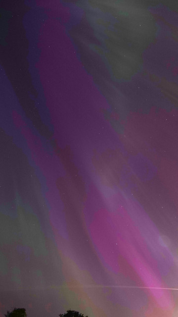A portrait shaped view of the night sky with purple and pink aurora streaks sweeping diagonally down from top left to bottom right, and greens and blues around
