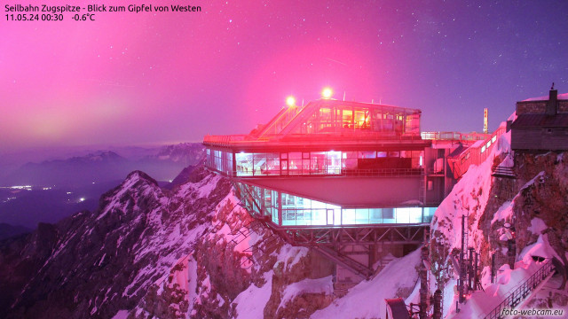 Nighttime view of the Zugspitze cablecar station near the summit with the entire scene tinted pink by the light of the aurora.
