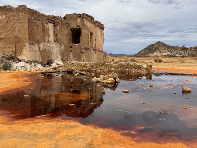 An abandoned mining building with a large puddle of dark red water in front. 