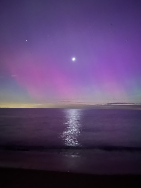 The moon shines through a wavy purple atmospheric curtain to reflect a long line in the dark waters beneath