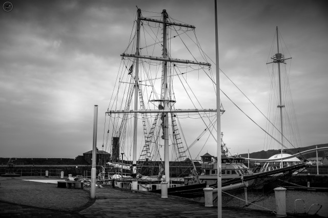 Monochrome shot of large two mast sailing ship at dock on stone paved harbour jetty