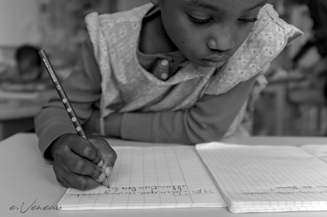 A schoolgirl copies a sentence on her lined notebook with a pencil.
