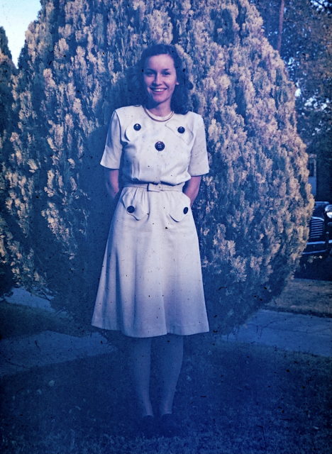 Young woman in a white dress standing in front of a bush. 